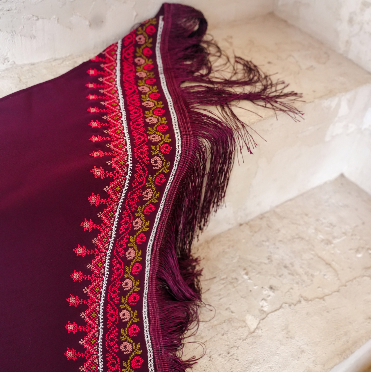 Purple fabric with intricate embroidery and fringes on a textured surface