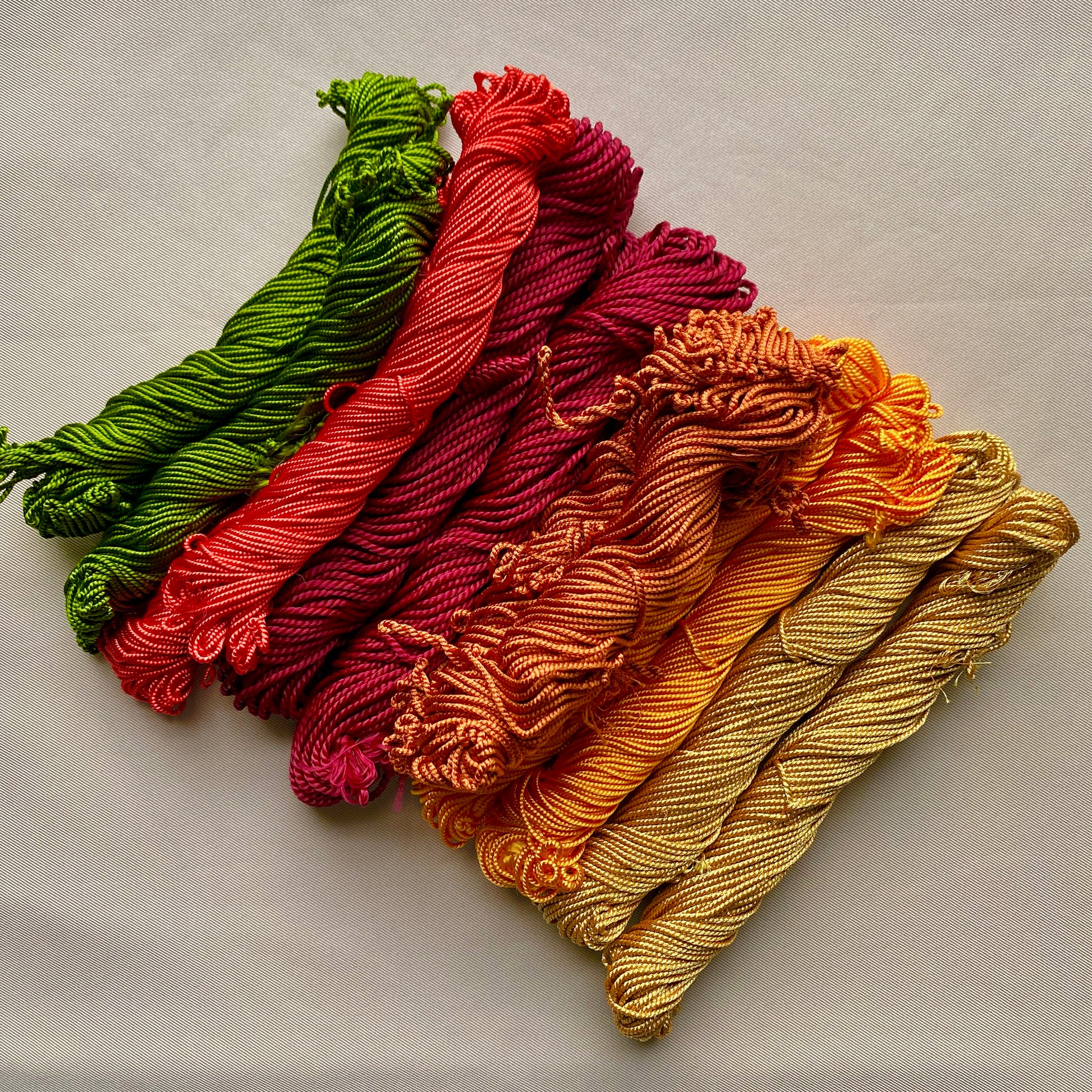 Five skeins of yarn in green, red, purple, orange, and yellow on a light gray background, tahriri thread, palestinian embroidery