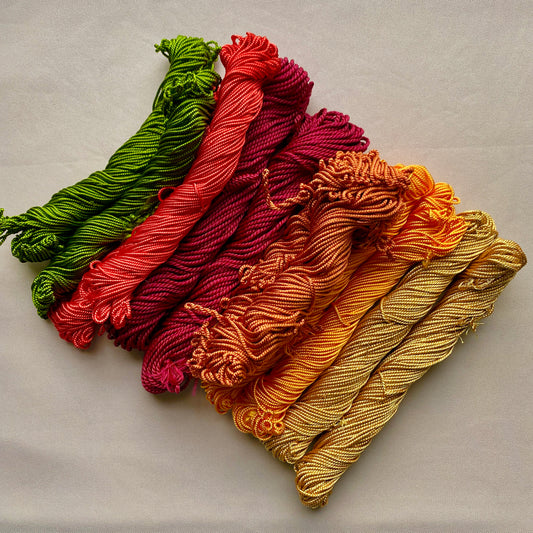 Five skeins of yarn in green, red, purple, orange, and yellow on a light gray background, tahriri thread, palestinian embroidery